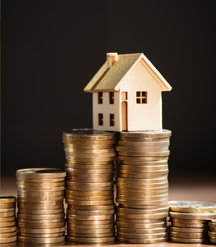 Maison miniature posée sur des piles de pièces représentant un financement immobilier rentable